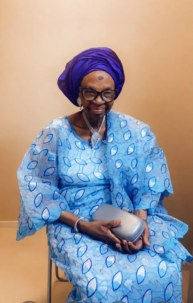 Deaconess Victoria Badejoko Lawoyin seated in a light blue patterned lace outfit with a purple gele.