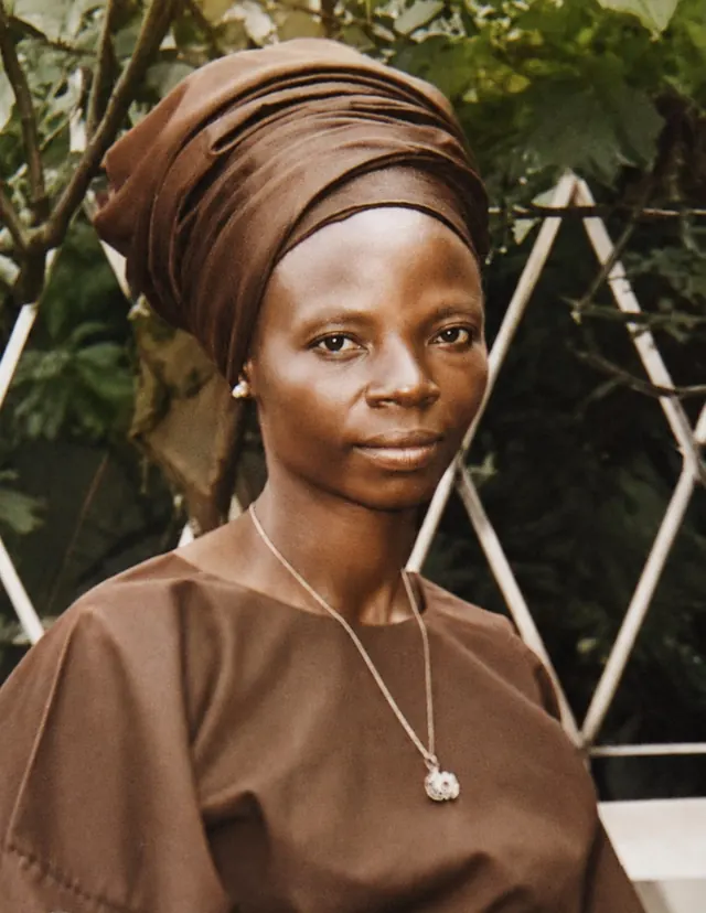 A young Deaconess Victoria Badejoko Lawoyin outdoors in a brown gele and matching blouse.